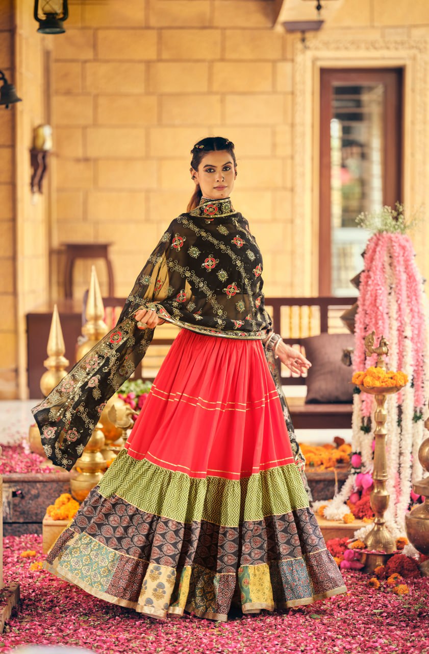 Full-length front view of a model in a red flared lehenga with chevron and printed block tiers, paired with a black embroidered dupatta