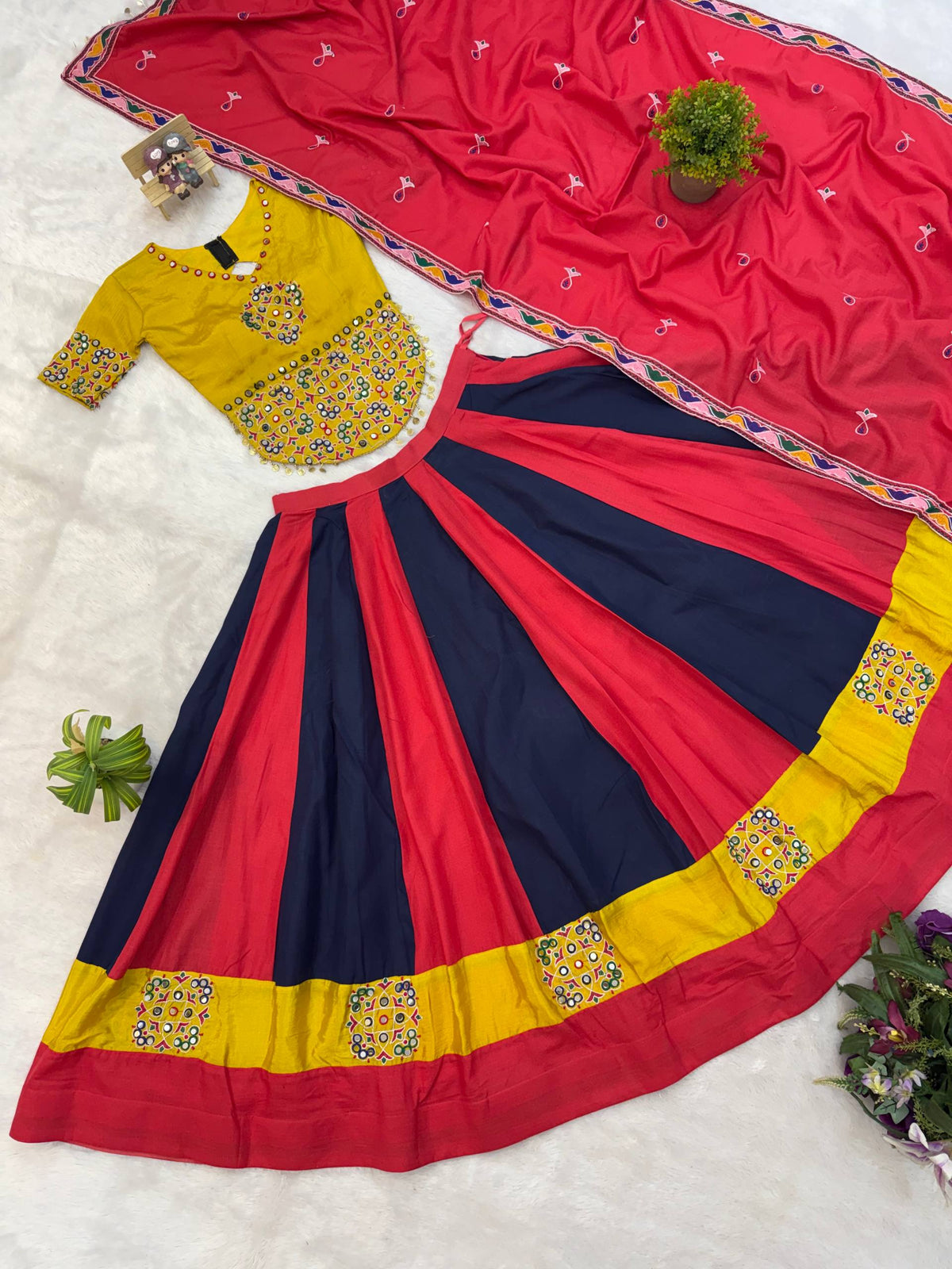 Flat lay view of red and navy blue panelled lehenga skirt, yellow embroidered blouse, and red dupatta with embroidered border