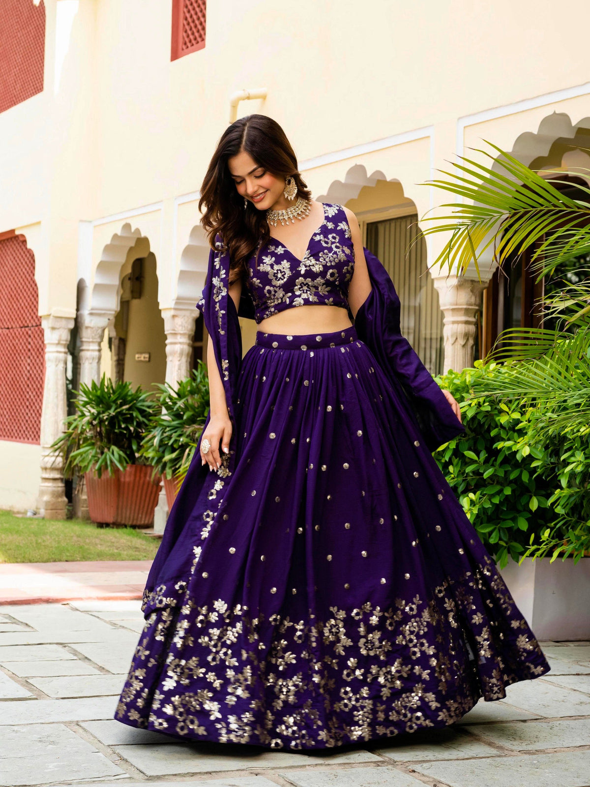 Side-angle view of model posing in royal purple embroidered sleeveless lehenga choli with gathered skirt