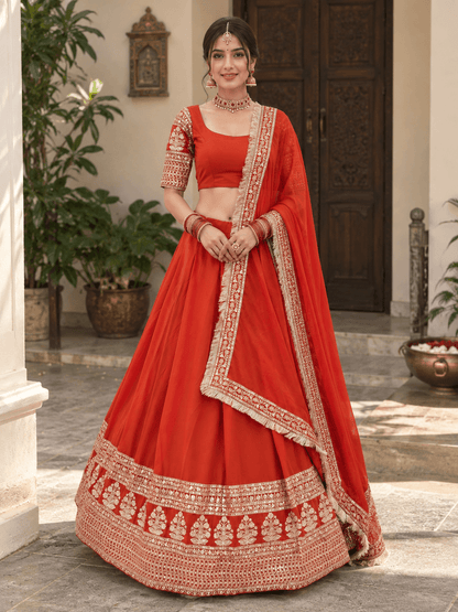 Full front view of model in a rust orange flared lehenga choli with gold tree motif border and fringe dupatta