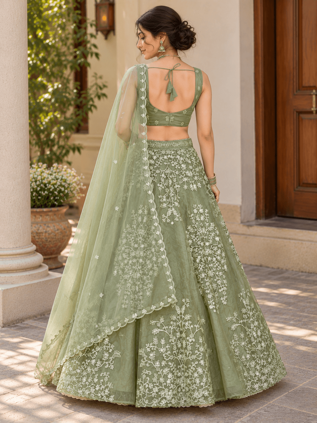 Back view of model wearing sage green lehenga choli with back tie-up blouse and floral embroidered skirt