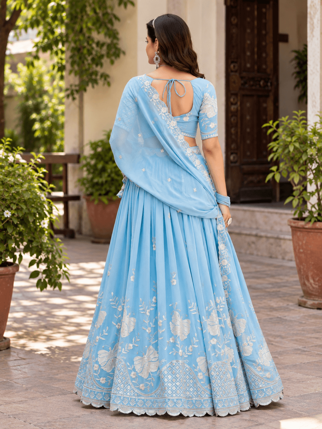 Back view of model wearing sky blue lehenga choli with back tie-up blouse and silver embroidered border dupatta