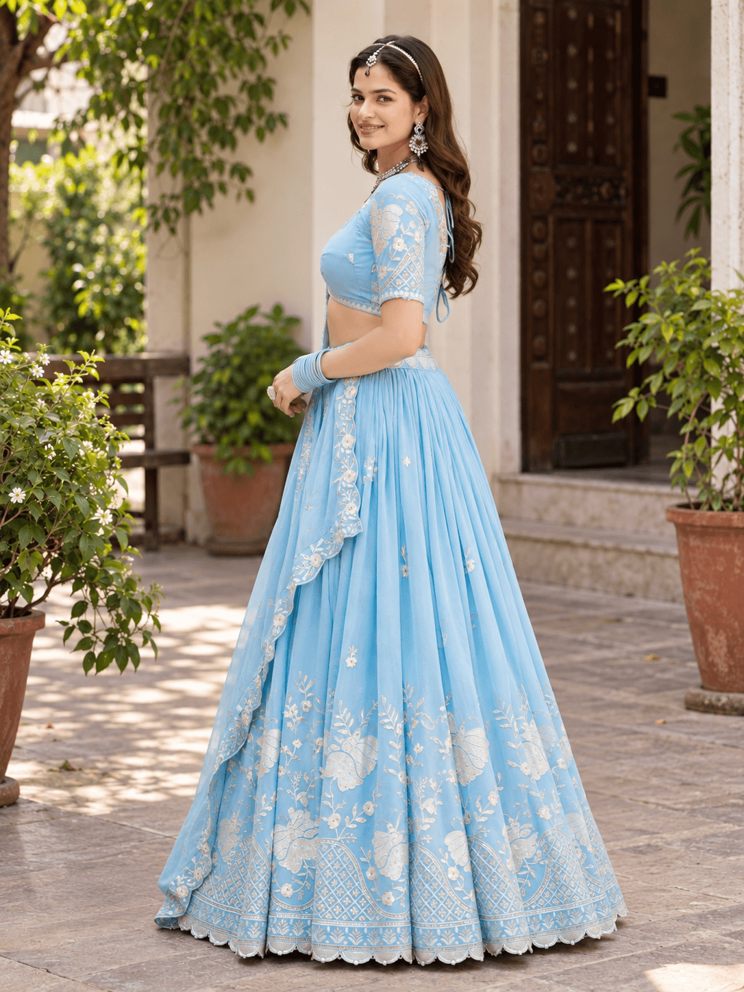 Side view of model wearing sky blue pleated lehenga with embroidered skirt border and matching dupatta