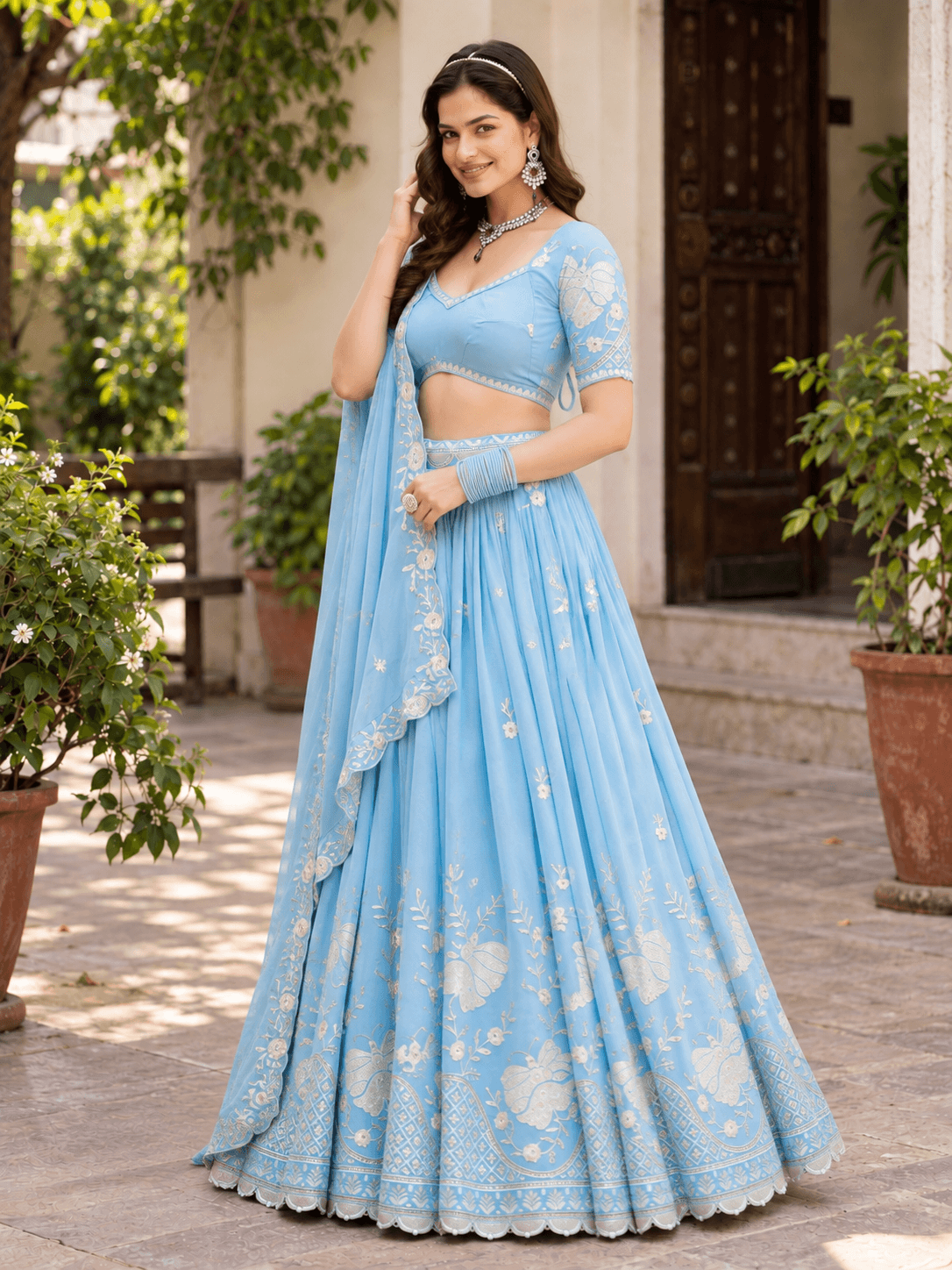Model posed in sky blue pleated lehenga choli with silver floral motifs and scalloped border hem