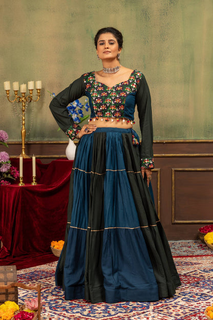 Model standing in dual-tone teal blue and black tiered lehenga skirt with full-sleeve floral embroidered blouse