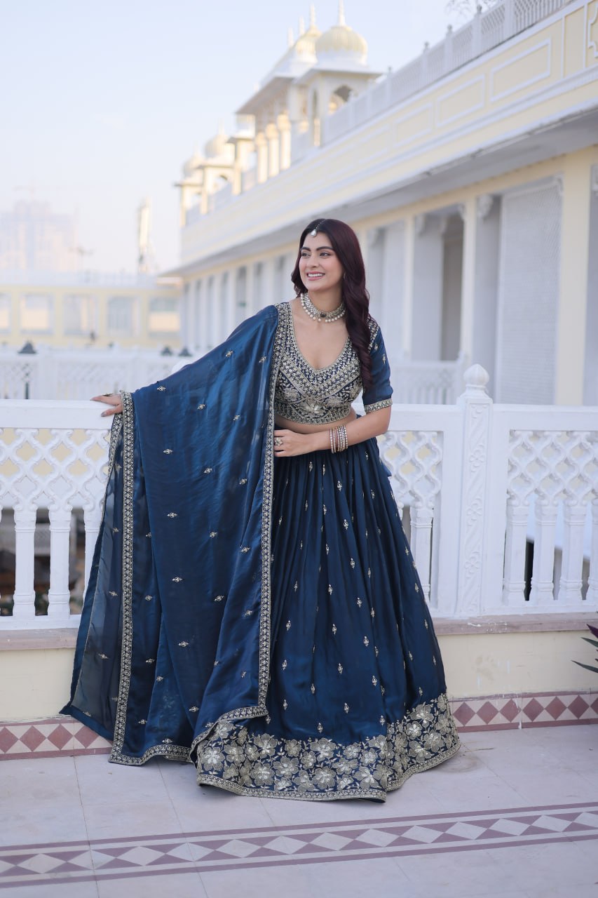 Full-length shot of model holding open the matching teal blue dupatta with embroidered lace border over a flared lehenga