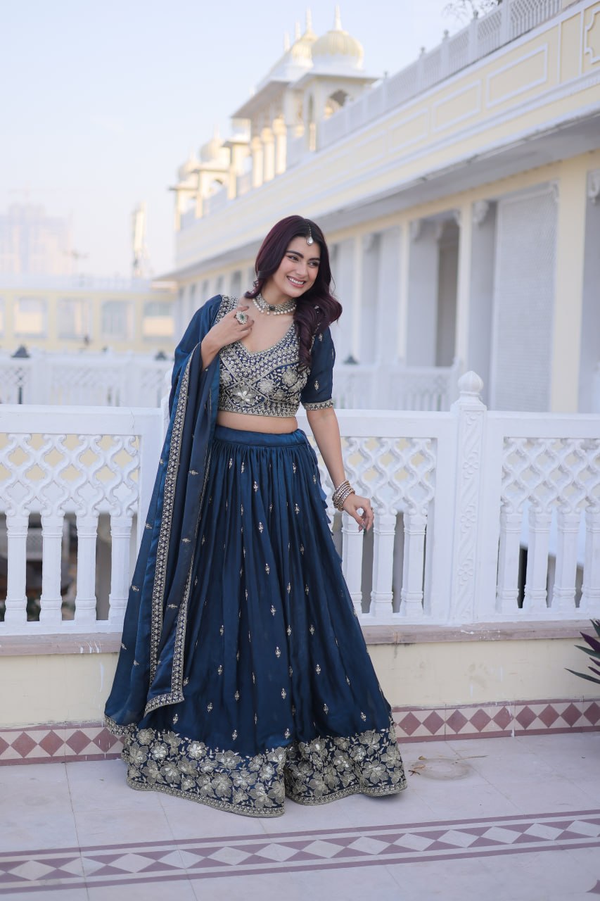 Standing full-length view of model wearing a teal blue embroidered lehenga choli set with one-side shoulder drape