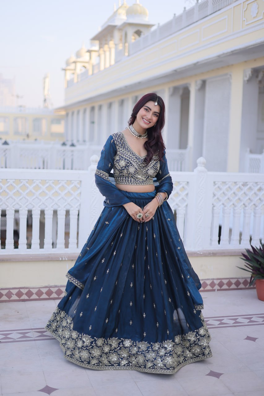 Full-length front view of a model in a teal blue pleated lehenga featuring a broad floral zari hemline and dupatta