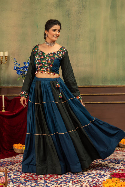 Three-quarter standing pose of model in tiered teal and dark green lehenga skirt with embroidered full-sleeve choli