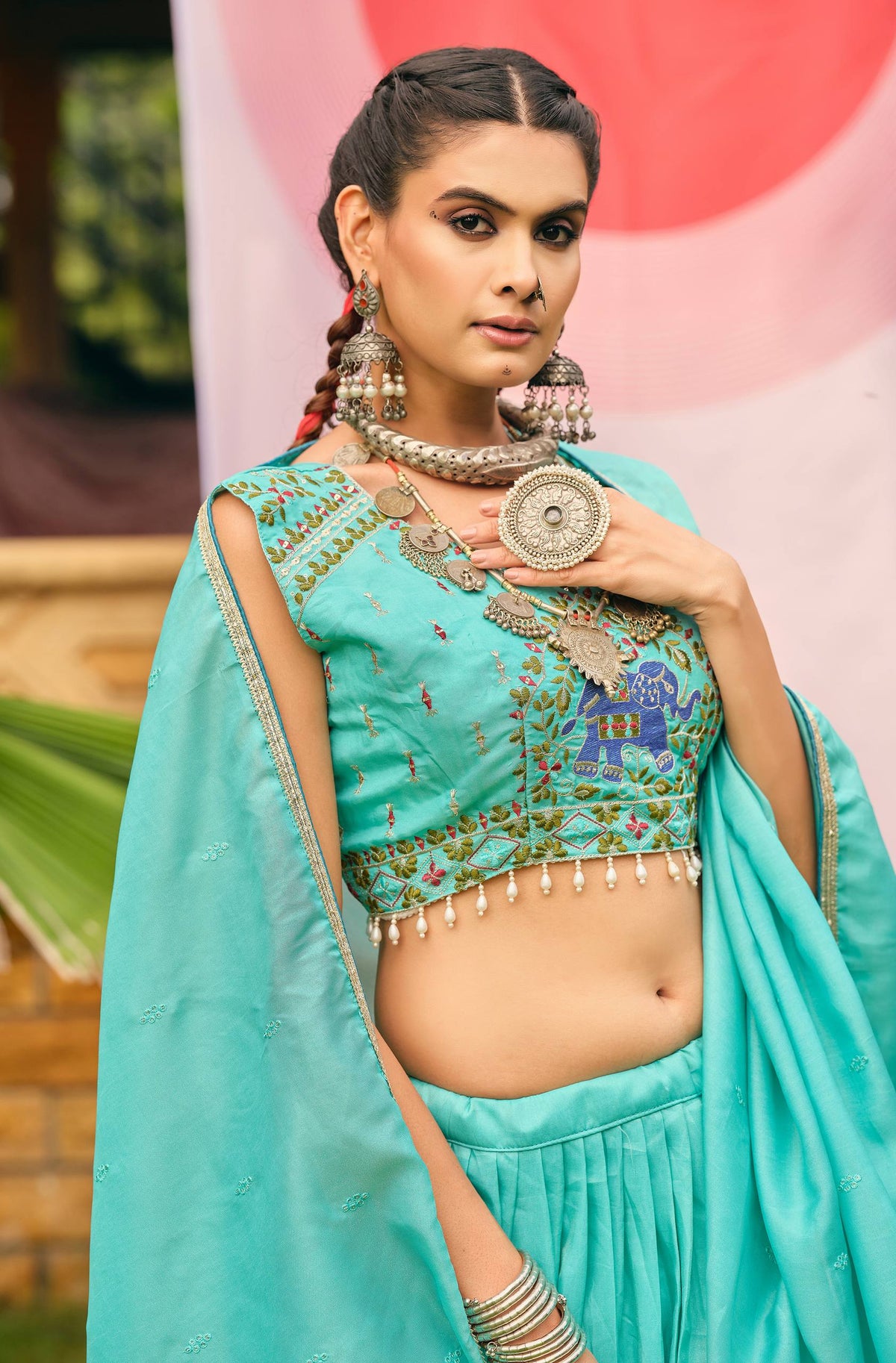 Mid-shot view of a turquoise blue sleeveless blouse with elephant embroidery and pearl drop fringe hem, styled with oxidized jewellery