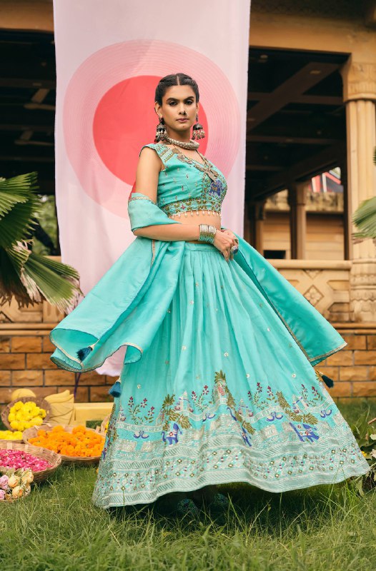 Outdoor full-length shot of a model wearing a turquoise blue pleated lehenga with embroidered elephant and tree motifs along the hem