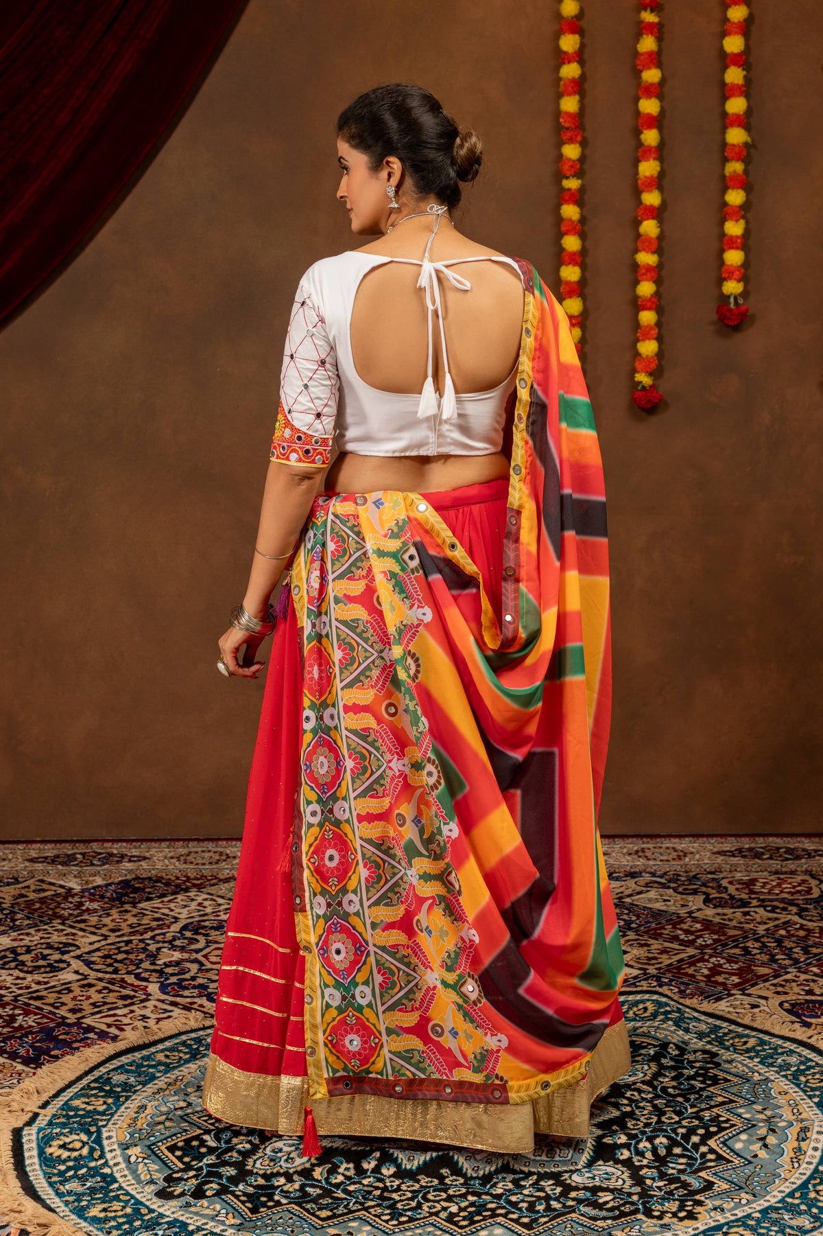 Rear view of a model showing the deep back cutout with tie-up tassels on a white blouse, styled with a draped multicolor dupatta.