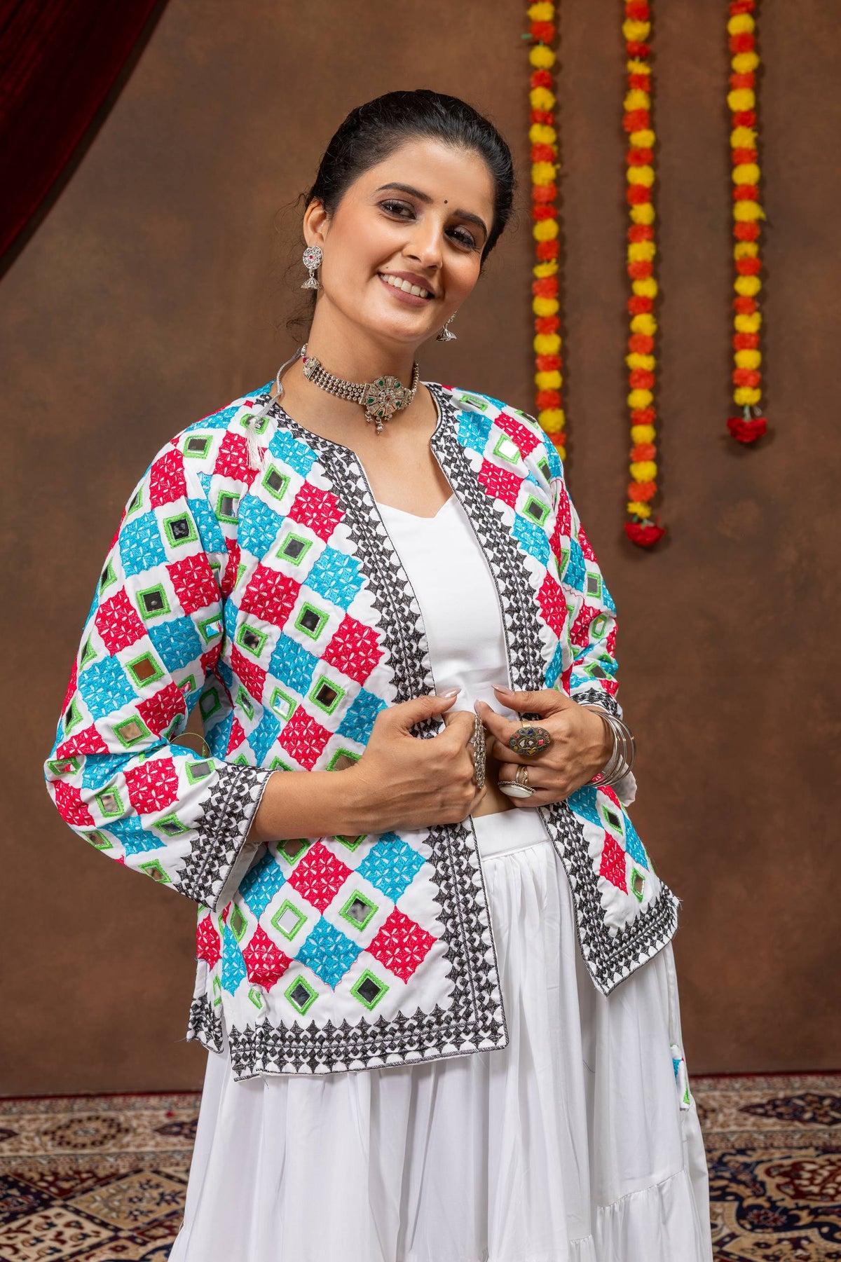 Mid-shot view of model wearing white crop top and white jacket with pink, blue, and green mirror embroidery
