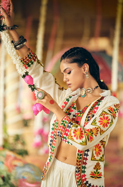 Mid-shot side view of a model in an open white collared jacket with colorful floral embroidery on the sleeve and front border