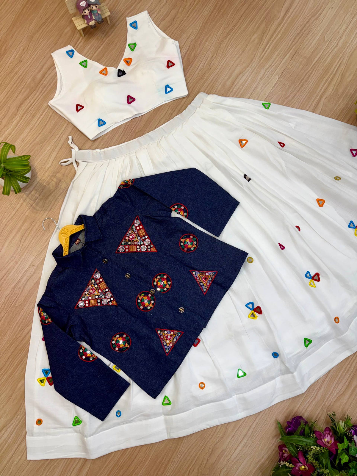 Flat lay view of white sleeveless crop top, pleated lehenga skirt, and buttoned blue embroidered jacket