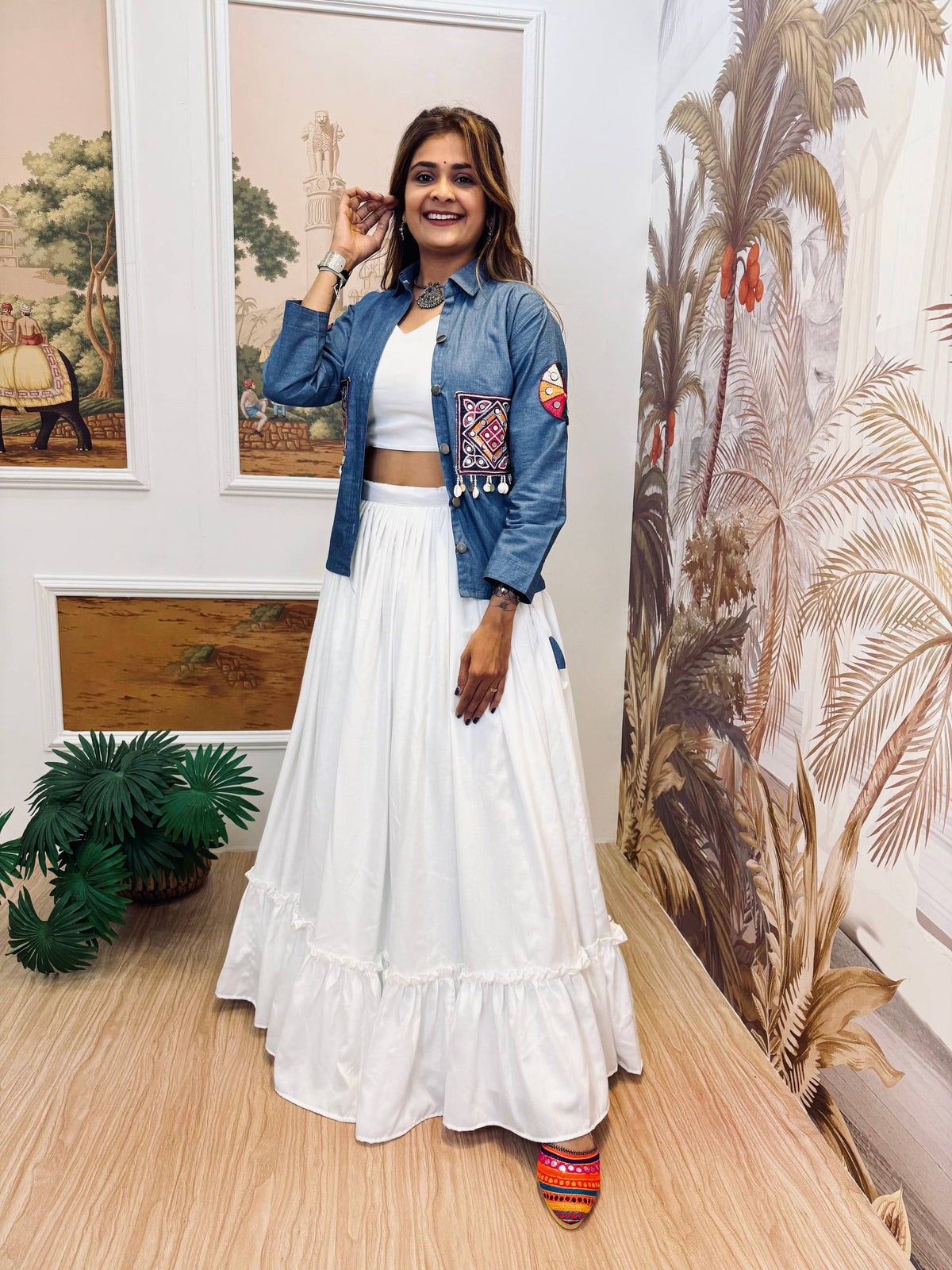 Model wearing a white flared ruffle lehenga and white crop top styled with an open blue embroidered jacket