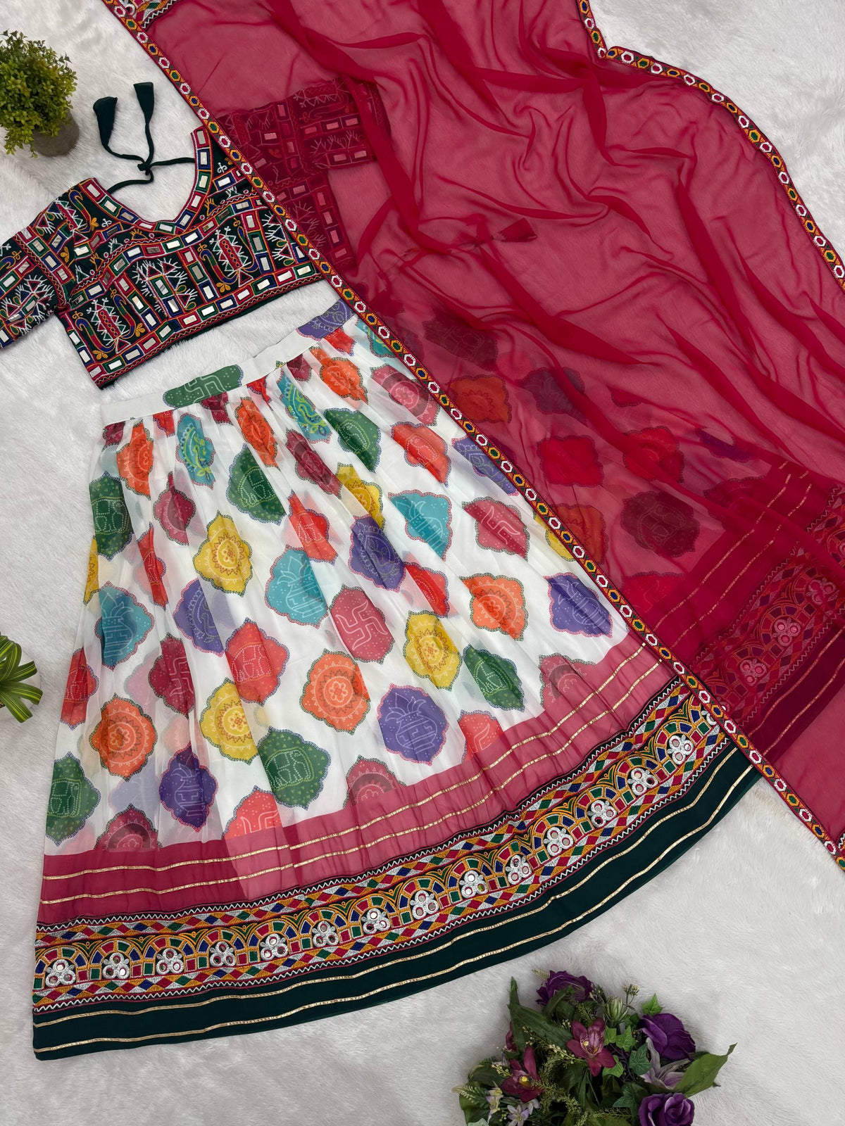 Flat lay view of white multicolor patola print lehenga skirt, embroidered green blouse, and pink dupatta