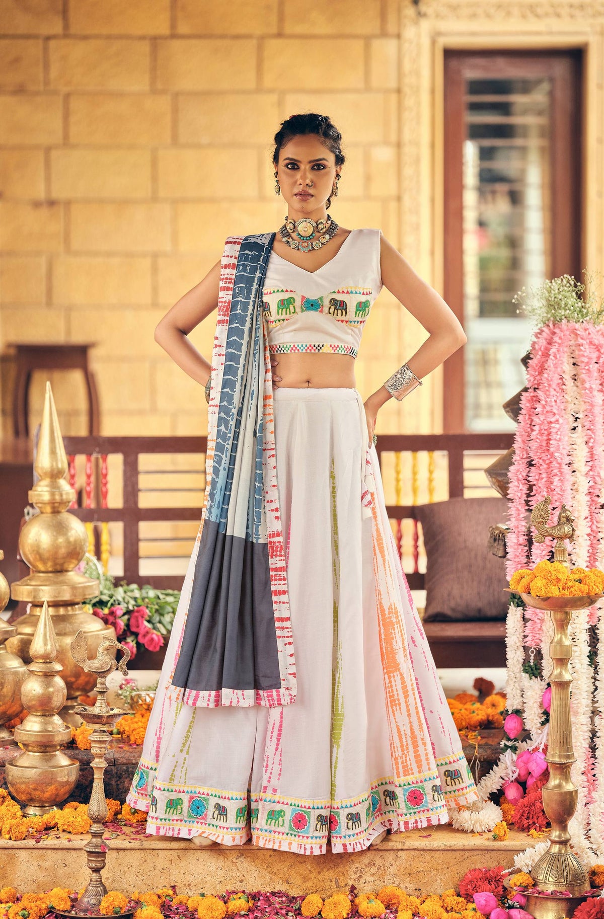 Full-length pose of model in a sleeveless white V-neck blouse and matching vertical tie-dye lehenga skirt