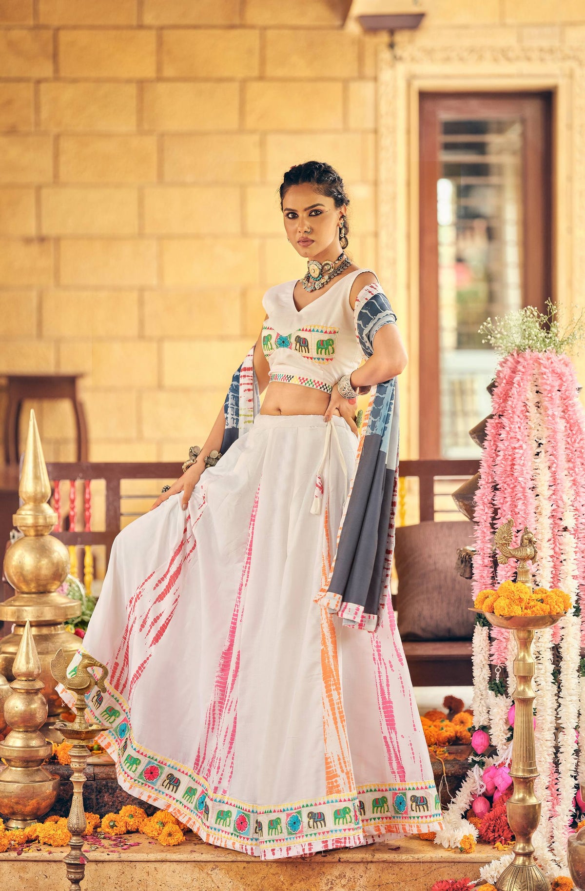 Model wearing a white flared lehenga with vertical tie-dye streaks, elephant motif border, and side-draped grey dupatta