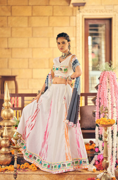 Model wearing a white flared lehenga with vertical tie-dye streaks, elephant motif border, and side-draped grey dupatta