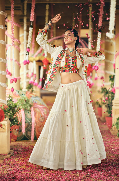 Full-length dynamic pose of model amidst falling rose petals wearing a white tiered lehenga, embroidered crop blouse, and jacket