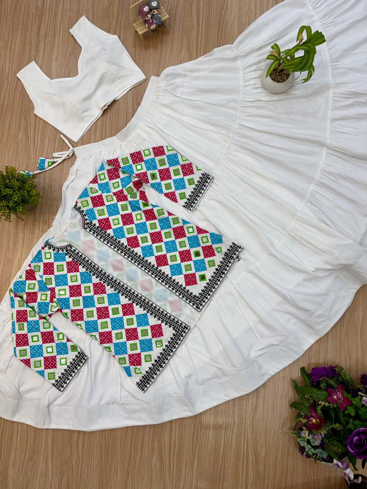 Flat lay view of white sleeveless crop top, tiered ruffled skirt, and geometric mirror embroidered jacket