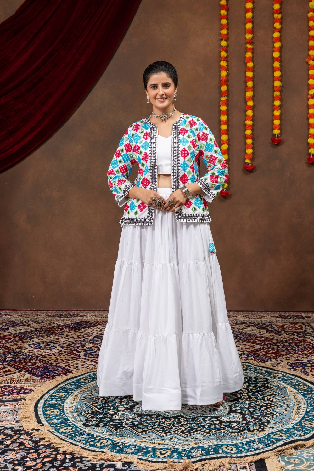 Full-length front view of model standing in white tiered lehenga choli set with open embroidered koti jacket
