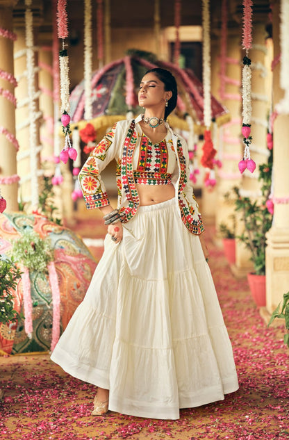 Full-length front view of a model in a tiered white lehenga skirt, embroidered crop top, and full-sleeve white jacket with tassels