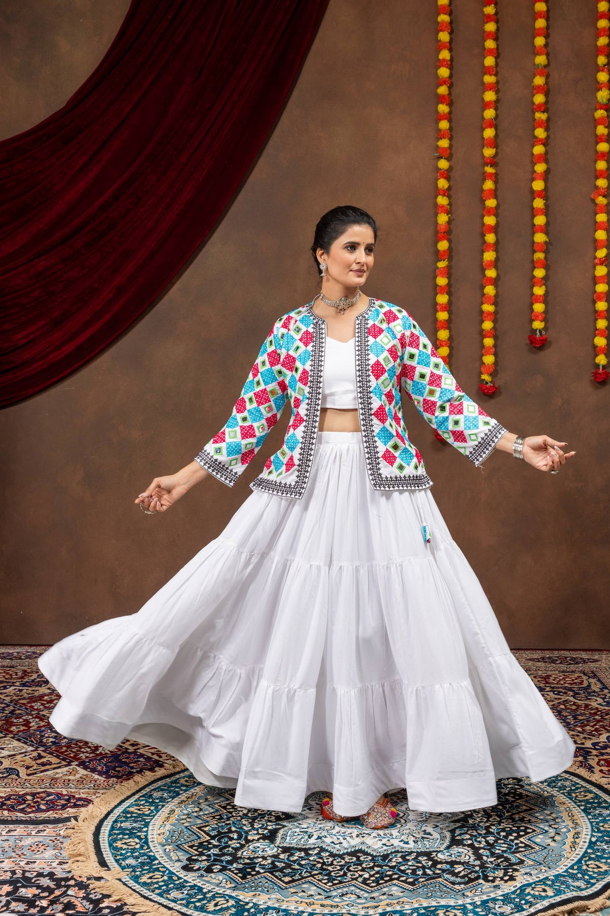 Model in open-arms pose wearing white tiered lehenga skirt and geometric mirror embroidered jacket