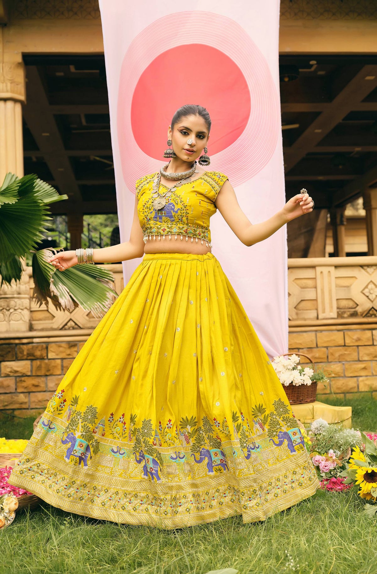 Outdoor full-length shot of a model in a yellow flared lehenga featuring embroidered blue elephant and tree motifs along the hem