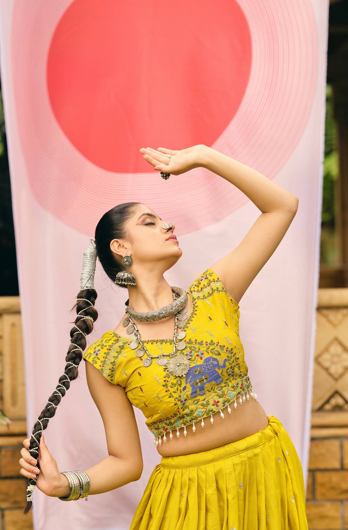 Expressive dance pose of model wearing a yellow cap-sleeve blouse with blue elephant thread embroidery and pearl trim